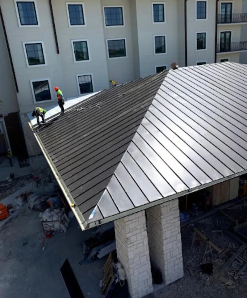 Crew installing standing seam metal roof panels on a commercial project in Elburn